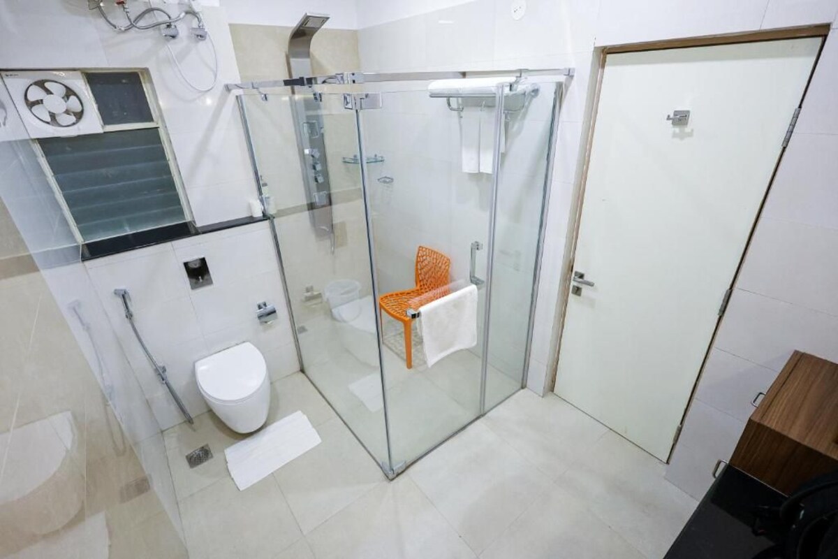 A modern bathroom with a glass-enclosed shower, a toilet, and a bench.