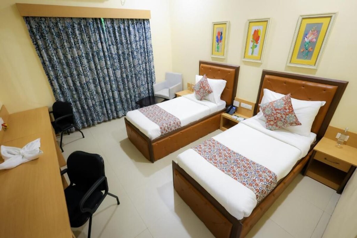 A hotel room with two beds, a desk, a chair, and a curtain.