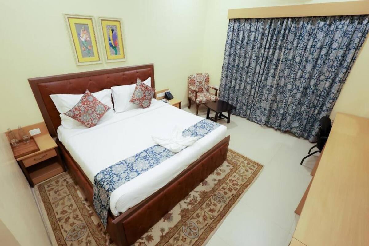 A neatly arranged hotel room with a large bed, a chair, a desk, and a window with curtains.