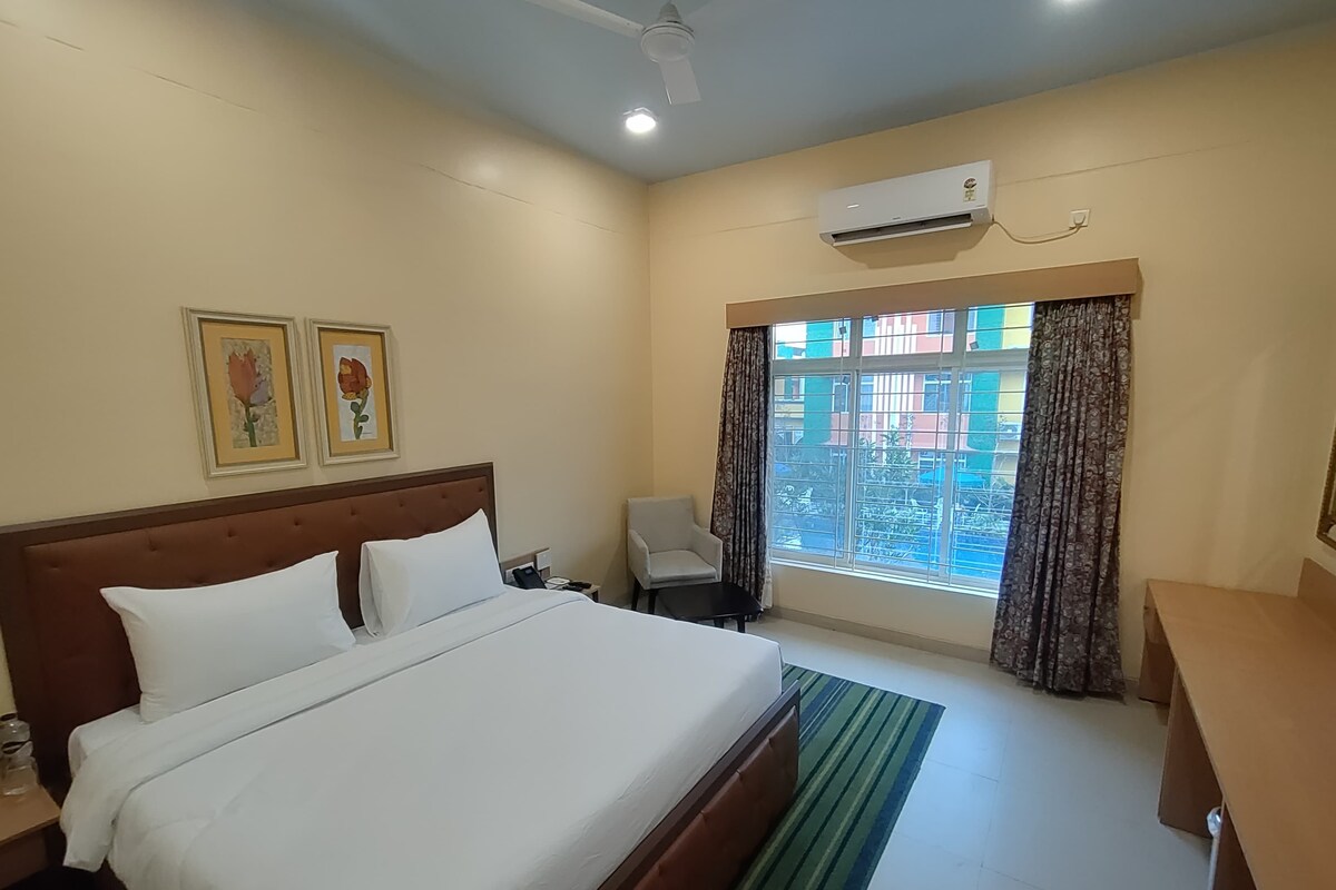 A hotel room with a bed, a chair, a desk, an air conditioner, and a window with curtains.