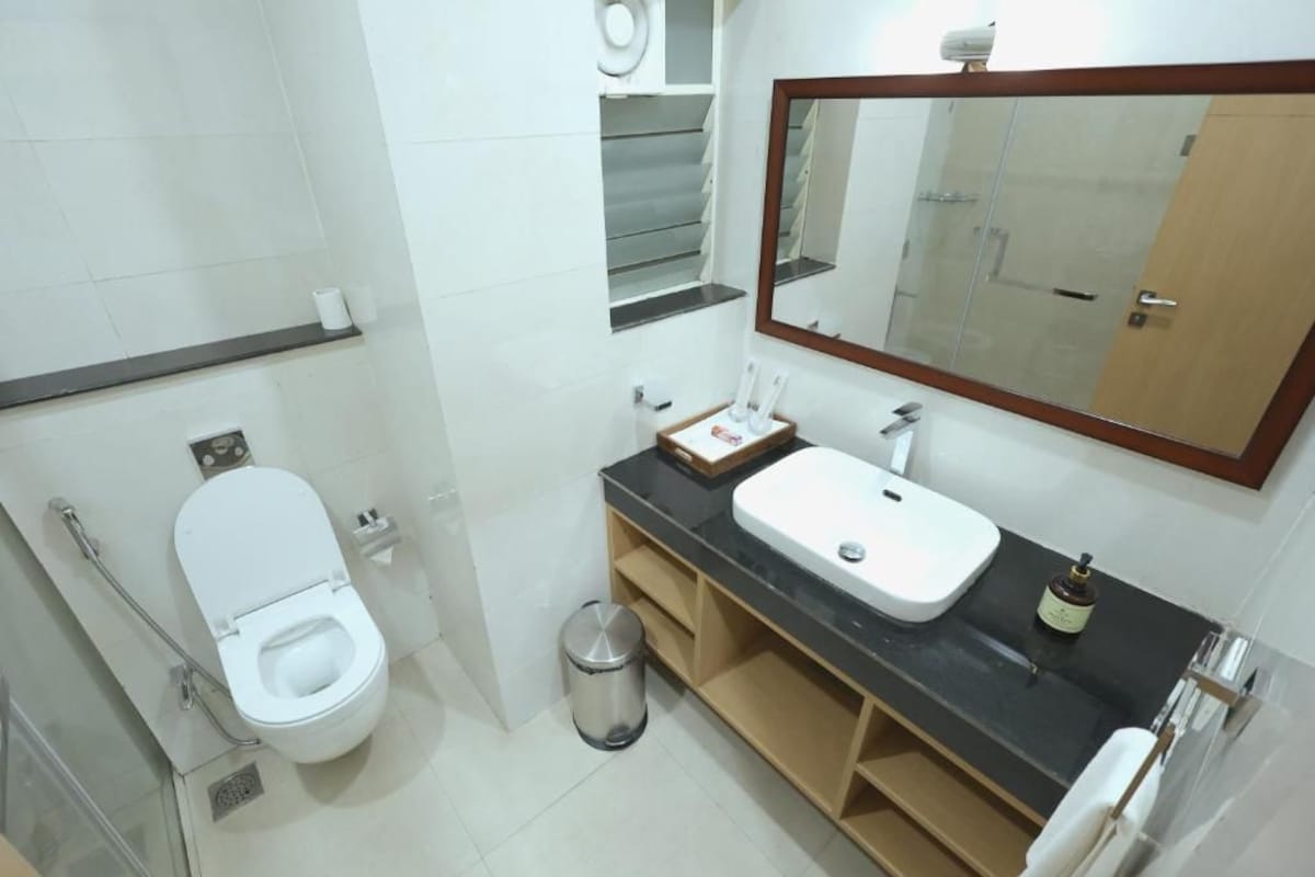 A modern bathroom with a toilet, sink, mirror, and a trash bin.