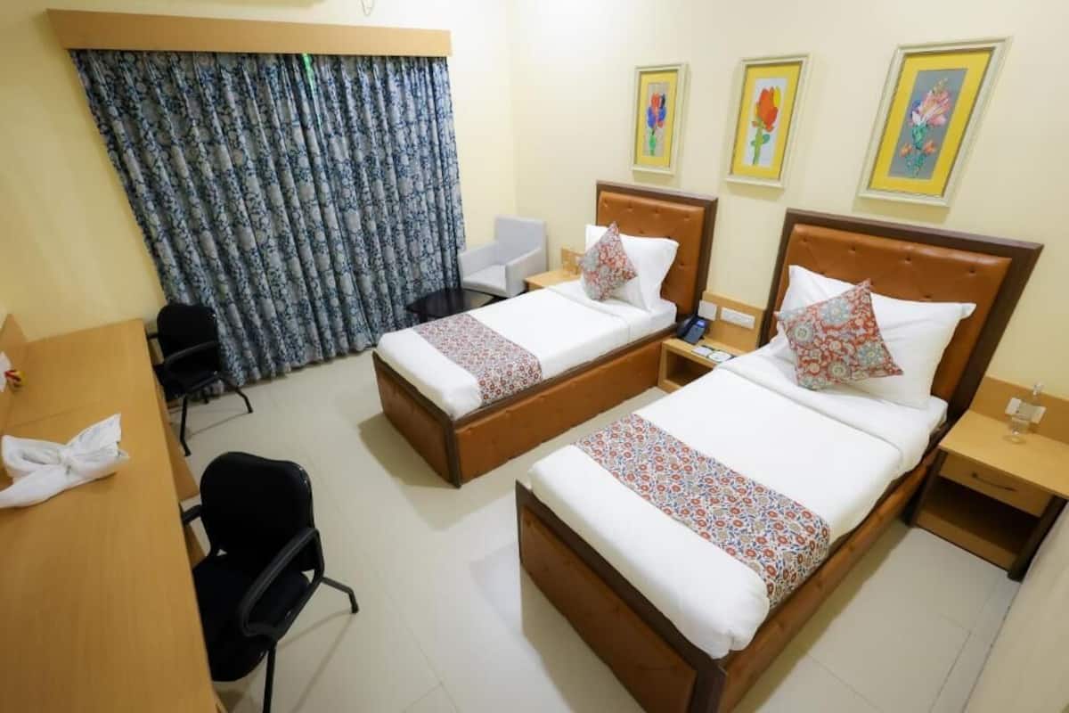 A hotel room with two beds, a desk, a chair, and a curtain.
