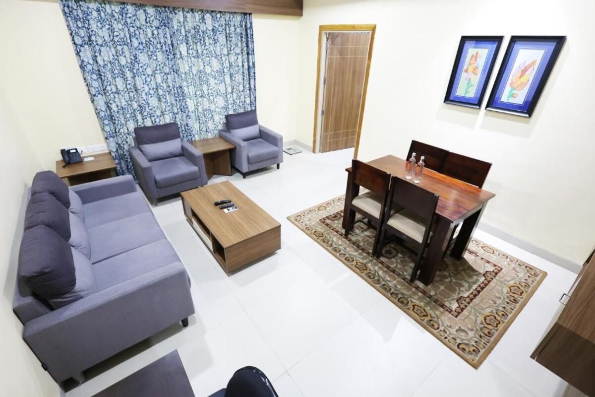 A living room with a sofa, armchairs, a coffee table, a dining table, and a patterned rug.