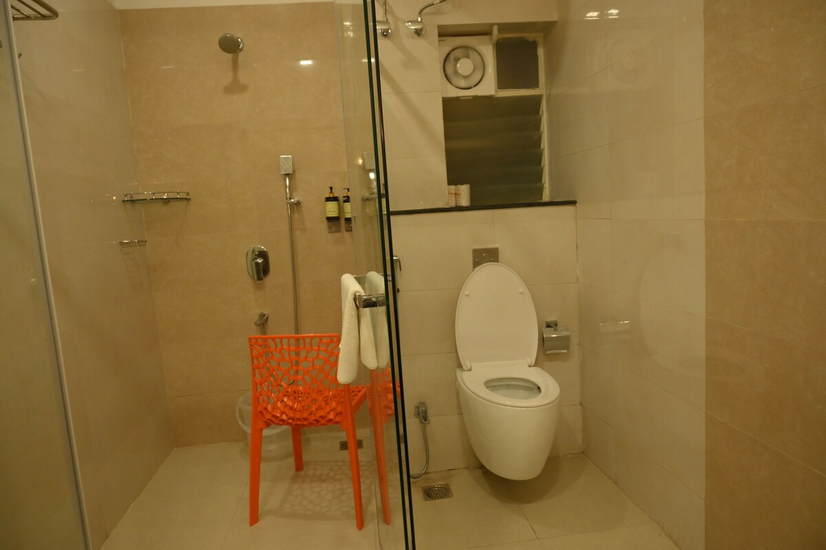 A bathroom with a glass-enclosed shower, a white toilet, and an orange chair.