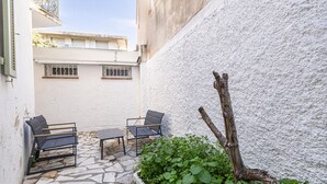 An outdoor seating area with two chairs and a table, a white textured wall, and a stone floor. - Le Windsor avec extérieur, pour un plaisir partagé (Cannes)