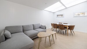 A modern living room with a grey sectional sofa, a small round table, and a dining area with wooden chairs and a white table. - Le Windsor avec extérieur, pour un plaisir partagé (Cannes)