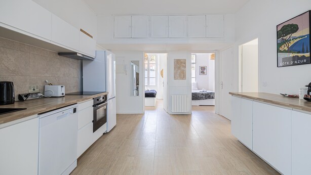 A modern kitchen with white cabinetry, a wooden countertop, and a view into the dining area. - Le Windsor avec extérieur, pour un plaisir partagé (Cannes)