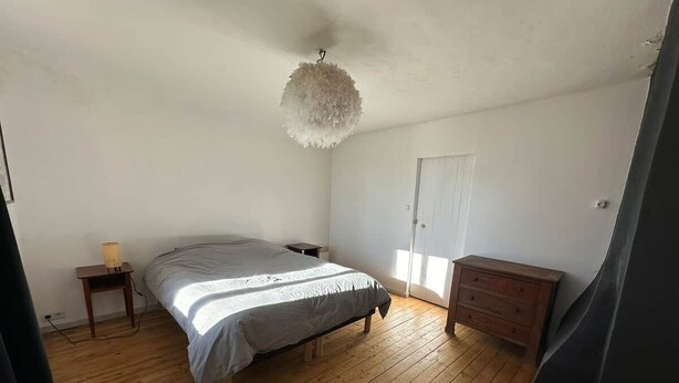 Un dormitorio con cama, suelo de madera, cómoda, lámpara y lámpara de techo.