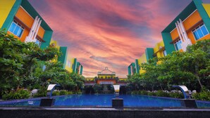 A modern building with a pool in the foreground and a colorful sky in the background. - Mayfair World Cup Village (Rourkela)