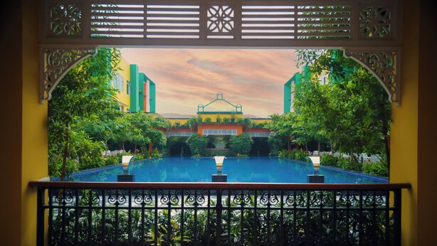 A view from a balcony with a pool, surrounded by ornate railings and lush greenery. - Mayfair World Cup Village (Rourkela)