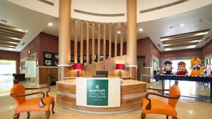 A reception area with a wooden reception desk, two orange chairs, and a sign for Mayfair World Cup Village Chhend, Rourkela. - Mayfair World Cup Village (Rourkela)