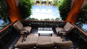 A balcony with two cushioned chairs and a table, overlooking a swimming pool. - Mayfair World Cup Village (Rourkela)
