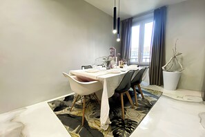 A dining area with a table set for four, a modern chandelier, and a view of the outside through large windows.