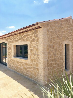 Un edificio de piedra con techo de tejas, ventanas grandes y entrada pavimentada.