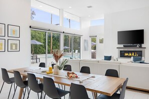 Un comedor moderno con una mesa de madera, sillas negras y vista a una piscina a través de amplios ventanales.