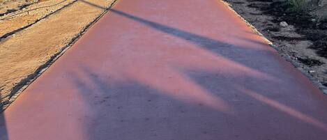 A paved pathway along a coastal area with red tents and a flag on the right, leading to the sea.