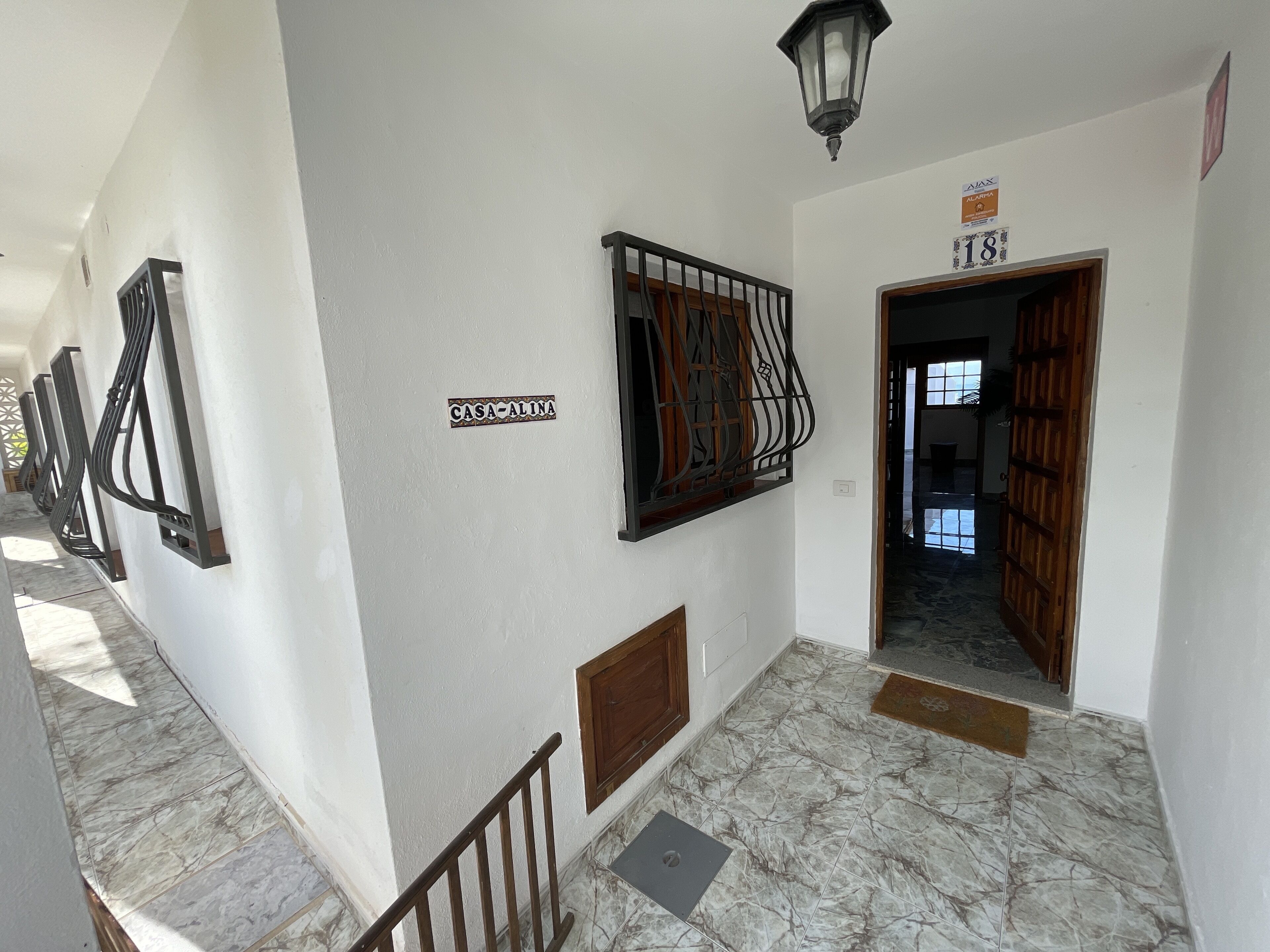 A hallway with a marble floor, a staircase with a wooden railing, and a door labeled "CASA-ALINA".