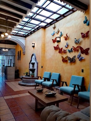 A lobby with a tiled floor, blue chairs, a wooden table, and a wall with butterfly decorations. - Room-room 3 for 2 People, Double Bed (Morelia)