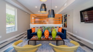 A modern living room with a blue sofa, orange and white patterned cushions, a coffee table, and yellow chairs. - Des Moines Designer 1BD 1BA Downtown Apartment (Des Moines)