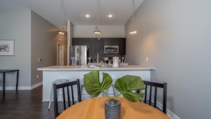 A modern kitchen with dark cabinets, stainless steel appliances, and pendant lighting. - Des Moines Designer 1BD 1BA Downtown Apartment (Des Moines)