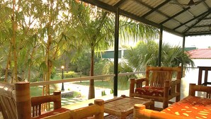 A covered outdoor seating area with wooden furniture and a view of a garden. - Forest Meadows Resort -Swiss In Salem (Salem)