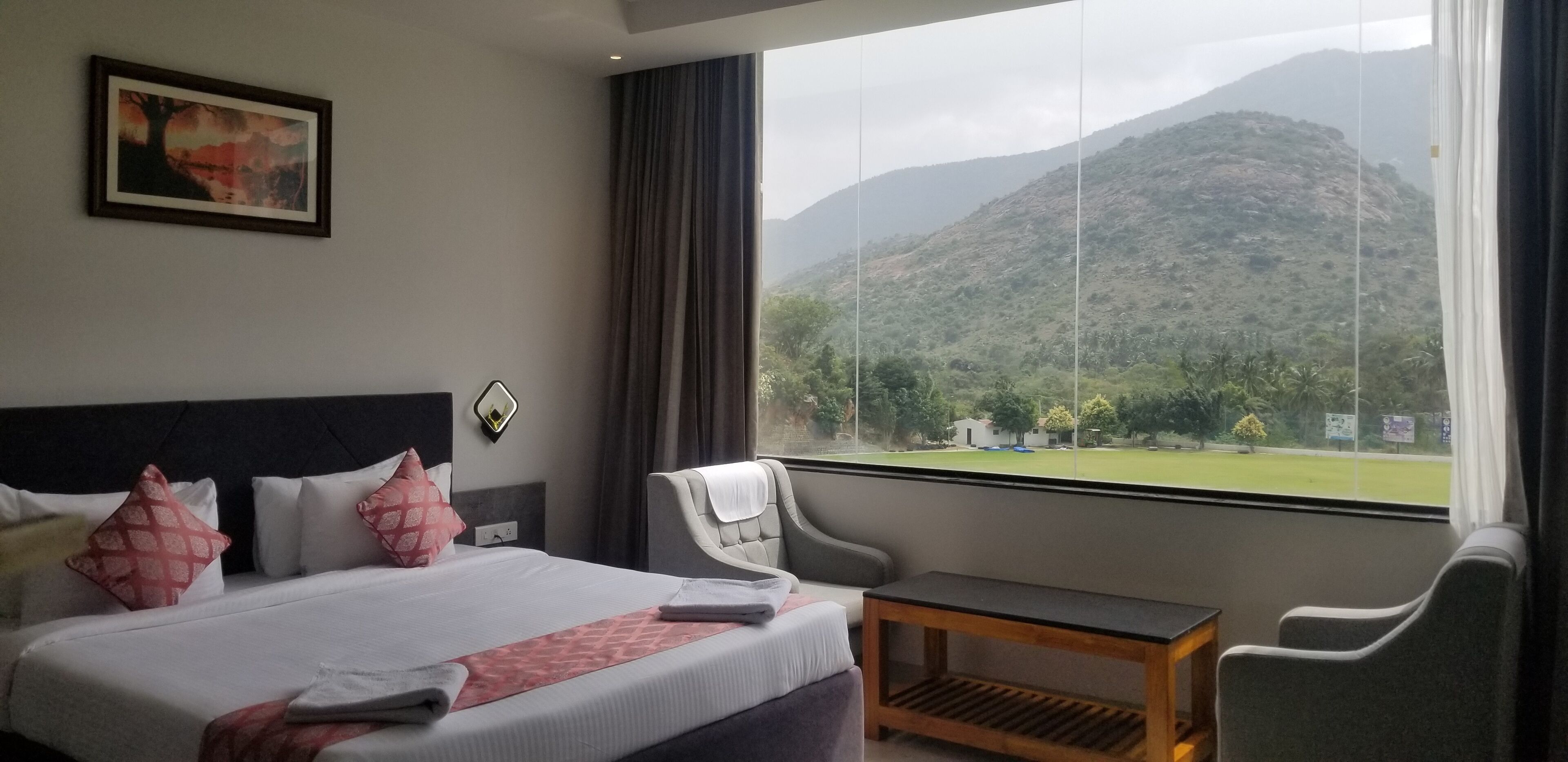 Habitación de hotel con cama, una silla, una mesita y ventana con vistas a la montaña.