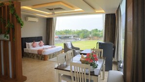 A hotel room with a bed, a desk with chairs, a TV, and a view of a green landscape. - Forest Meadows Resort -Swiss In Salem (Salem)