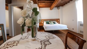 Una habitación con una cama, una mesa con mantel de encaje y un jarrón con flores.
