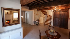 Un interior rústico con vigas de madera a la vista, chimenea, una escalera y un comedor con una mesa dispuesta para dos.