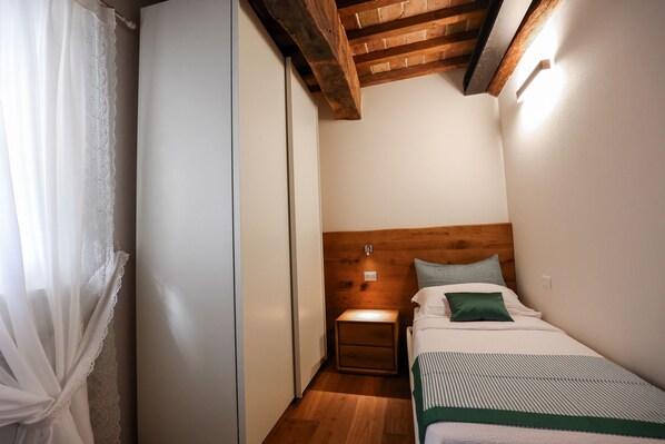 A small, cozy bedroom with a wooden headboard, a bedside table, and a bed with a green pillow.