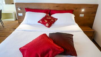 A neatly made bed with white and red bedding, a wooden headboard, and a bedside table with a drawer.