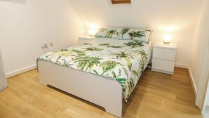 Una camera da letto con un letto, due comodini con lampade, un pavimento in legno e uno specchio fissato alla parete.