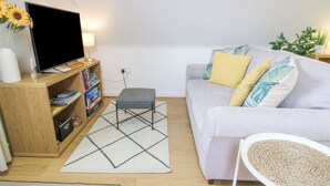 Un soggiorno moderno con un divano, un poggiapiedi, una TV su un mobile in legno, una libreria e una pianta in vaso.