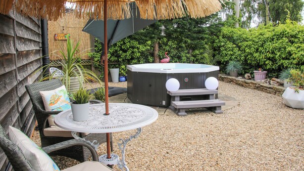 Un'area patio con un ombrellone di paglia, mobili in vimini, una vasca idromassaggio e piante in vaso.