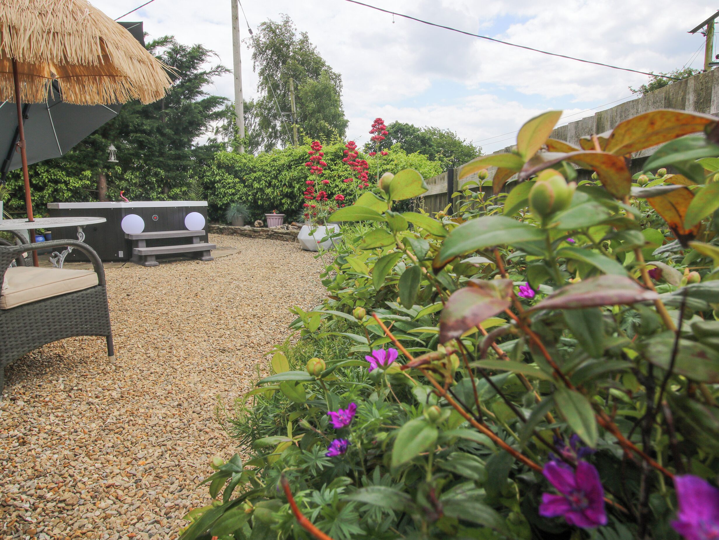 A garden area with a thatched umbrella, a bench, and a table with a cushion.