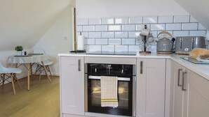 Una cucina compatta con mobili bianchi, forno integrato, un piccolo tavolo con sedie e un tostapane.
