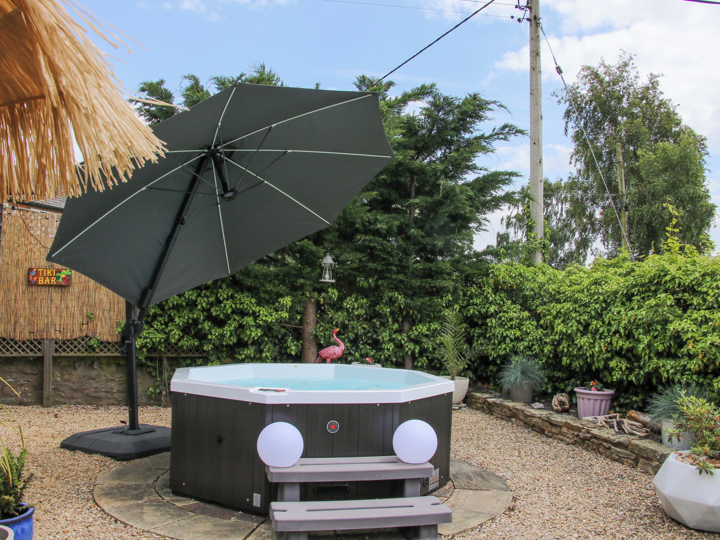 A hot tub with steps and a large umbrella in a garden setting.