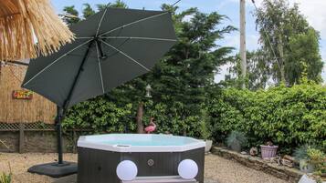 A hot tub with steps and a large umbrella in a garden setting.