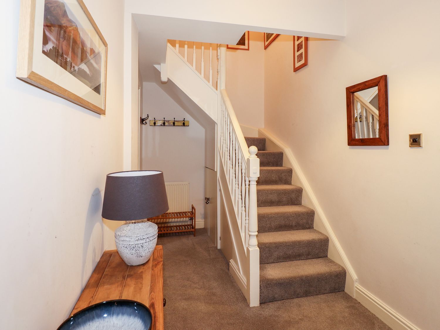 A staircase with carpeted steps and white railings, a wooden bench with a lamp, and a coat rack with hangers.