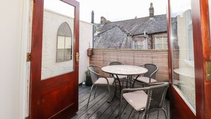 Una terraza de madera con una mesa redonda y cuatro sillas, una puerta de madera, y vistas a casas vecinas.