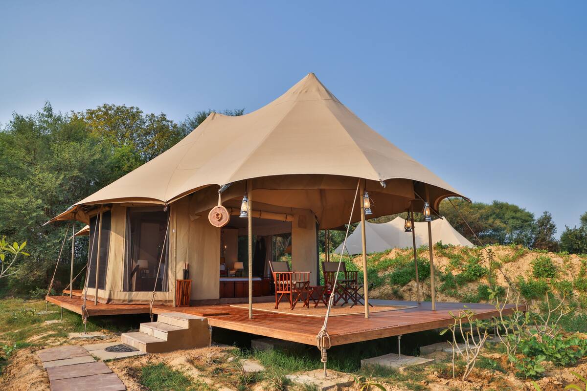 A tented accommodation with a wooden deck, seating area, and a view of the surrounding landscape.