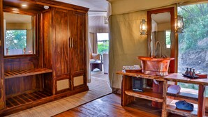 Ein Zimmer mit Holzboden, einem großen Spiegel, einer Holzkommode und einem Tisch mit Spüle aus Kupfer.