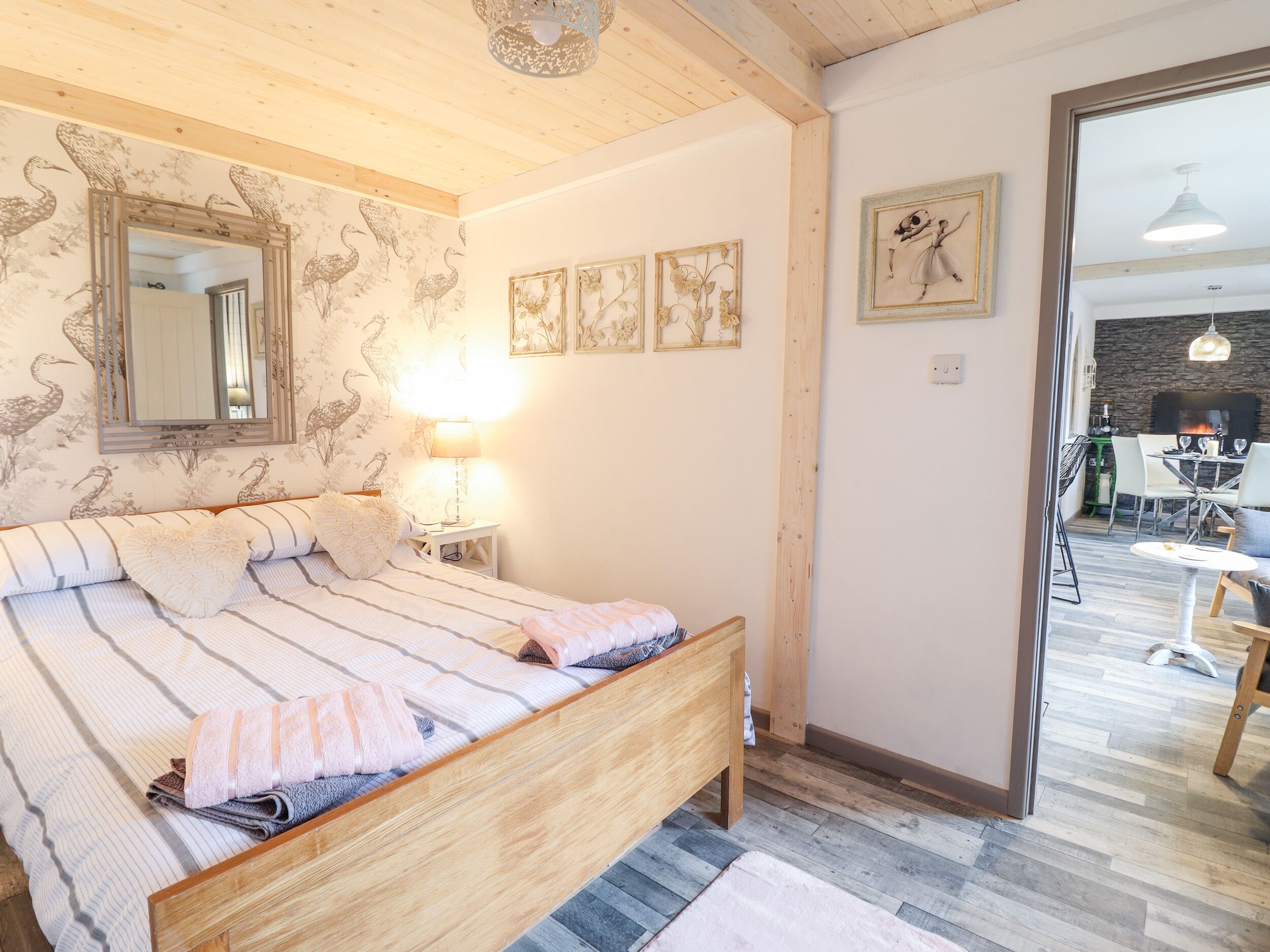 Ein Schlafzimmer mit einem hölzernen Bett, einem Spiegel, einer Lampe und einem Essbereich, der durch eine offene Tür sichtbar ist.