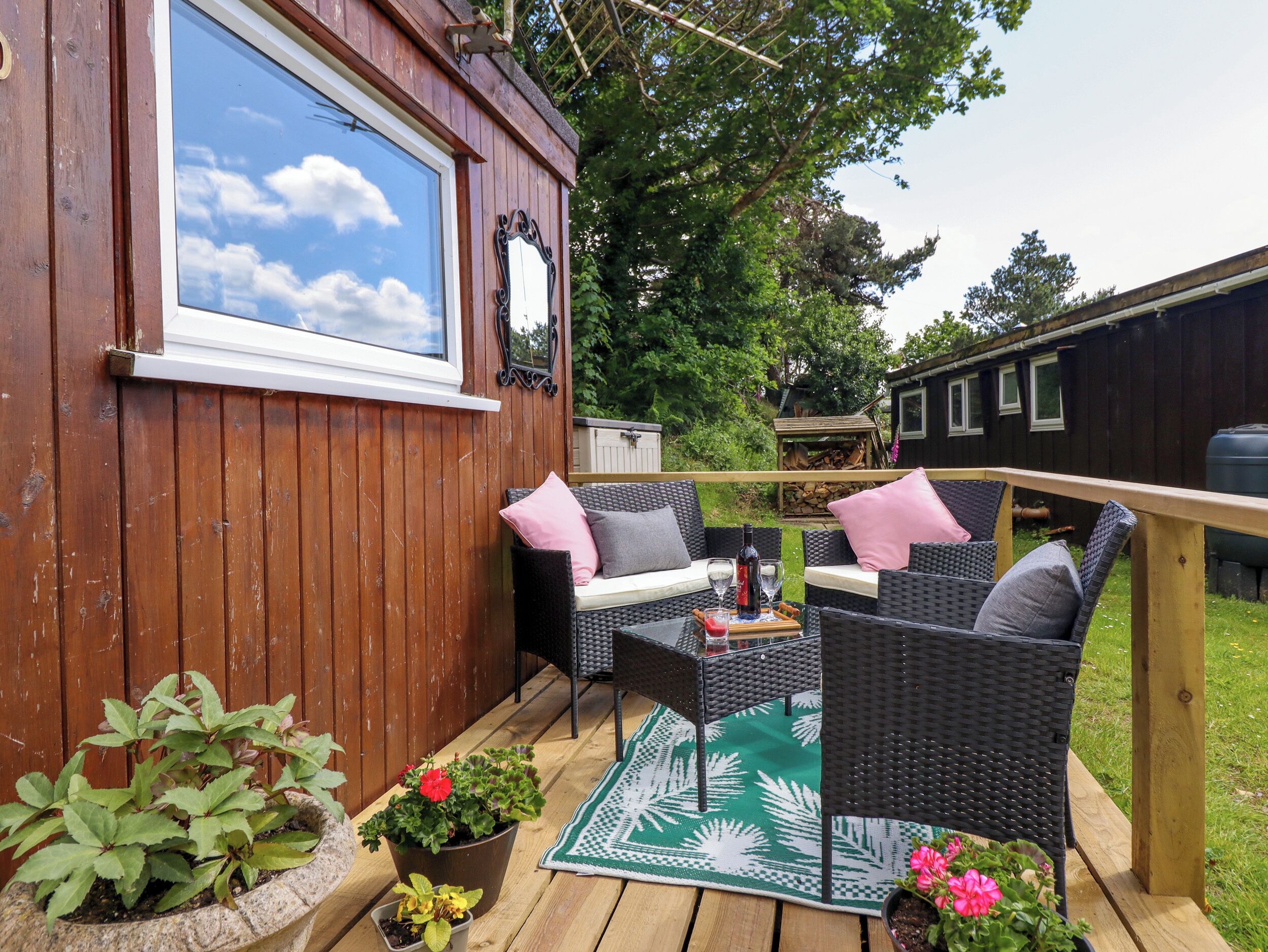 A wooden deck with wicker furniture, a window, and potted plants.