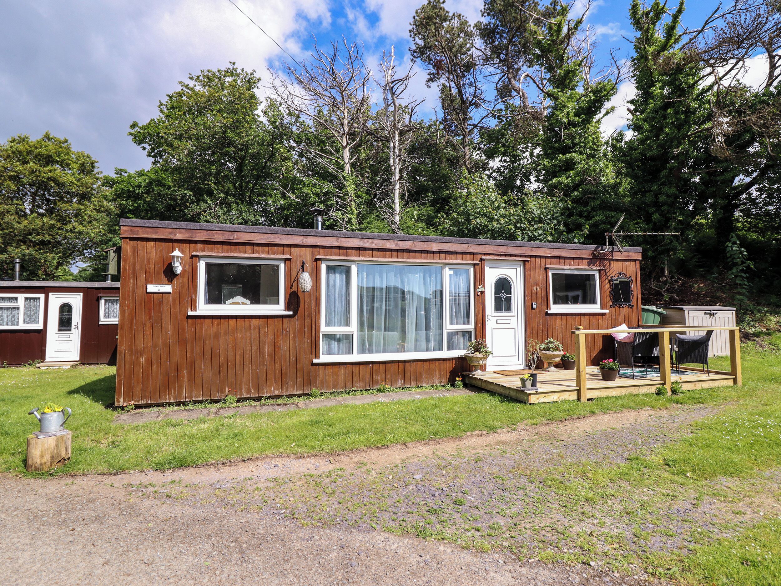 A wooden mobile home with a front porch, large windows, and a small deck area.