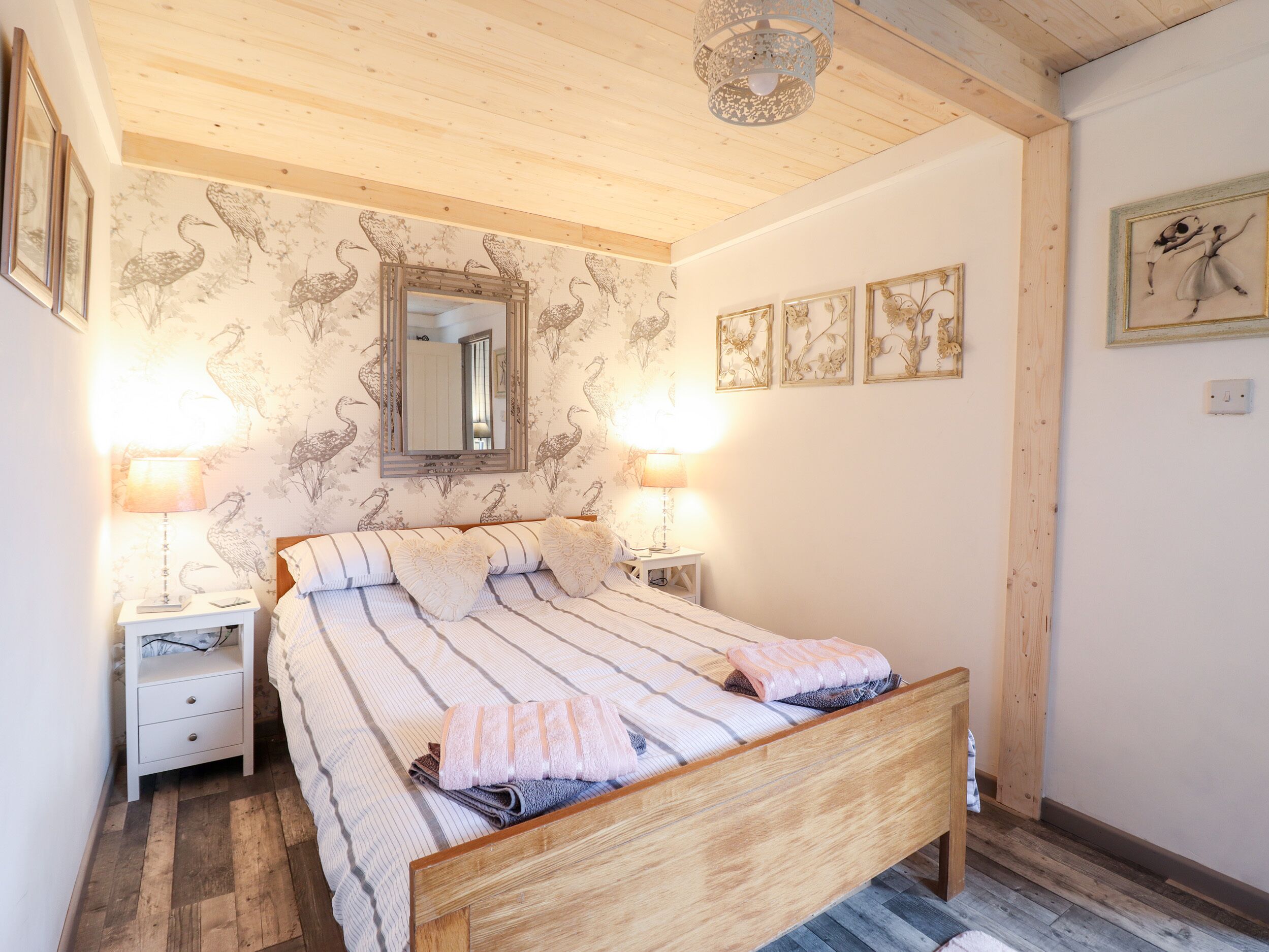 A bedroom with a wooden bed, two bedside tables with lamps, a mirror, and wall-mounted artwork.