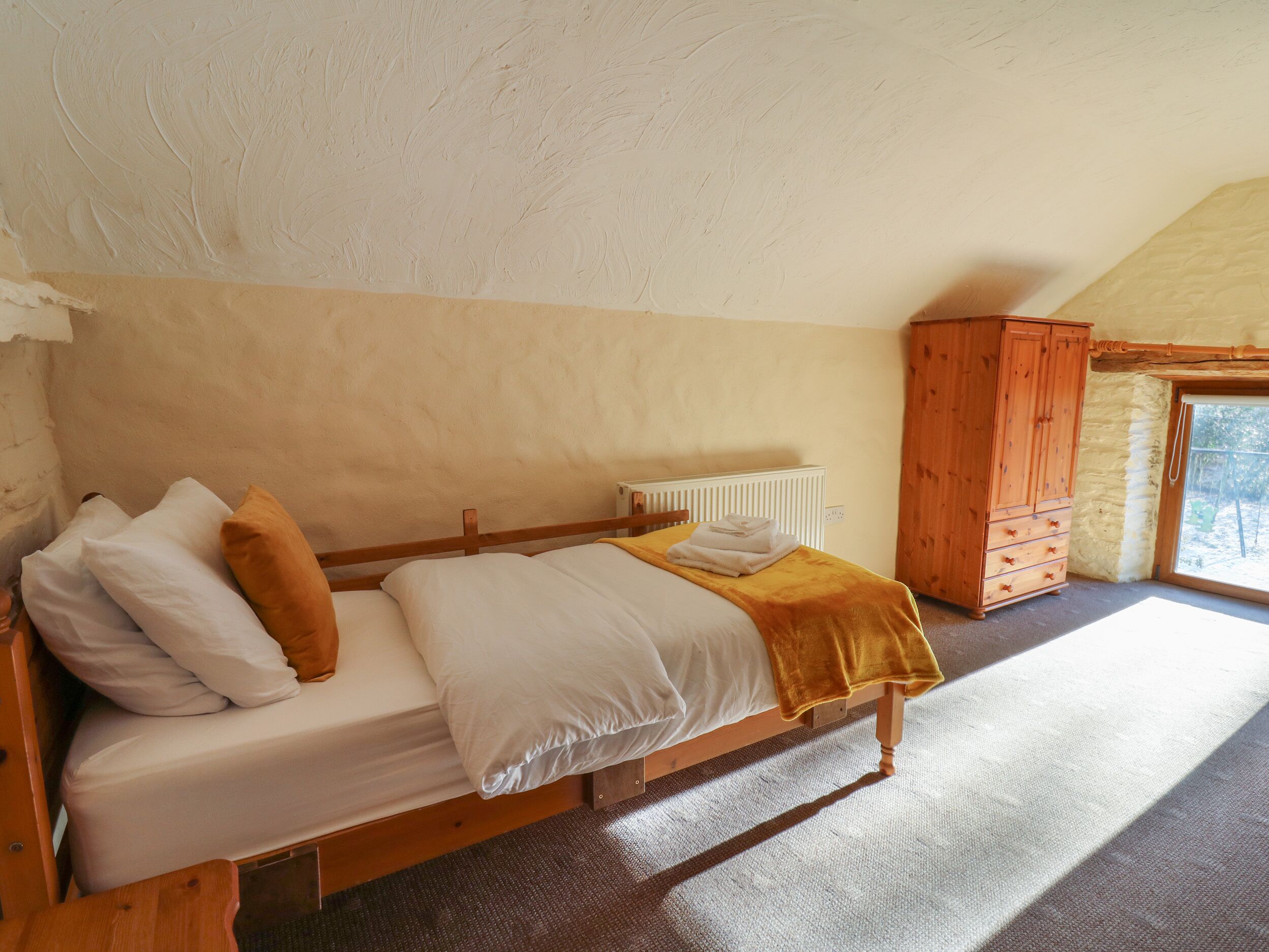 Ein Schlafzimmer mit einem hölzernen Bett, weißer Bettwäsche, einer gelben Tagesdecke, einem Holzschrank und einem Heizkörper.