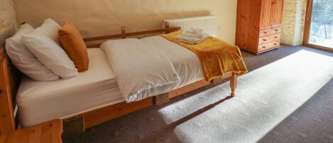 Ein Schlafzimmer mit einem hölzernen Bett, weißer Bettwäsche, einer gelben Tagesdecke, einem Holzschrank und einem Heizkörper.