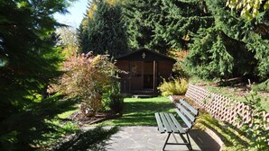 Una baita di legno con un portico, immersa nel verde e con un sentiero in pietra che conduce a una panchina.