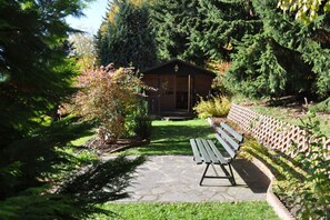 Eine Holzhütte mit Veranda, umgeben von dichtem Grün und einem Steinweg, der zu einer Bank führt.